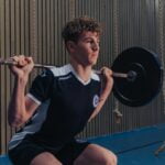 A young man squatting with a barbell in a gym, showcasing fitness and wellness.