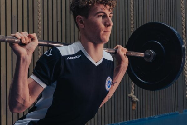 A young man squatting with a barbell in a gym, showcasing fitness and wellness.