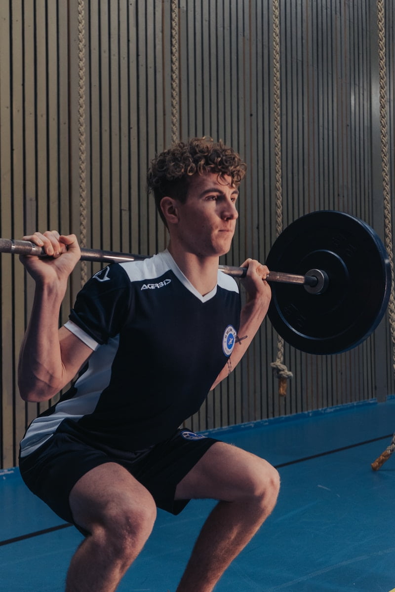 A young man squatting with a barbell in a gym, showcasing fitness and wellness.