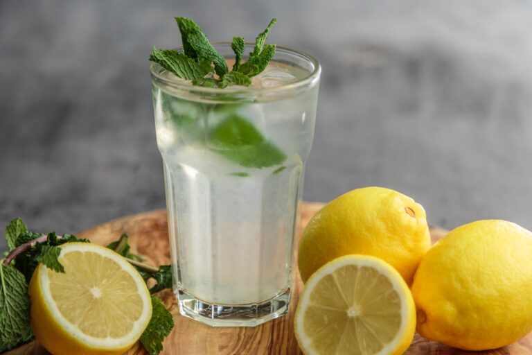 A refreshing glass of lemonade with mint leaves on a wooden cutting board, offering rejuvenating diet advice for anti-aging tips.