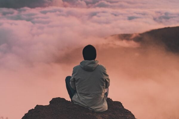 A man sitting on top of a mountain overlooking the clouds, finding solace in the serene beauty of nature.