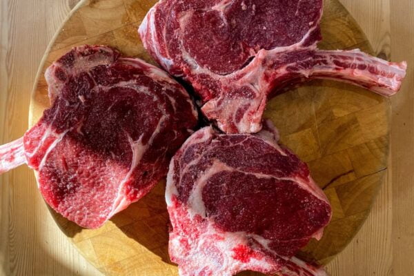 Three steaks, aged to perfection, are sitting on a wooden table.