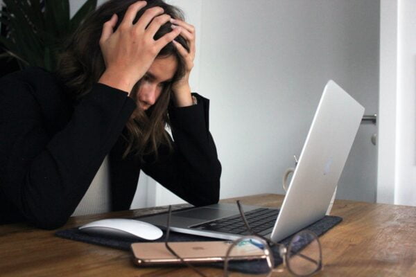 A woman is holding her head in front of a laptop while seeking wellness tips.