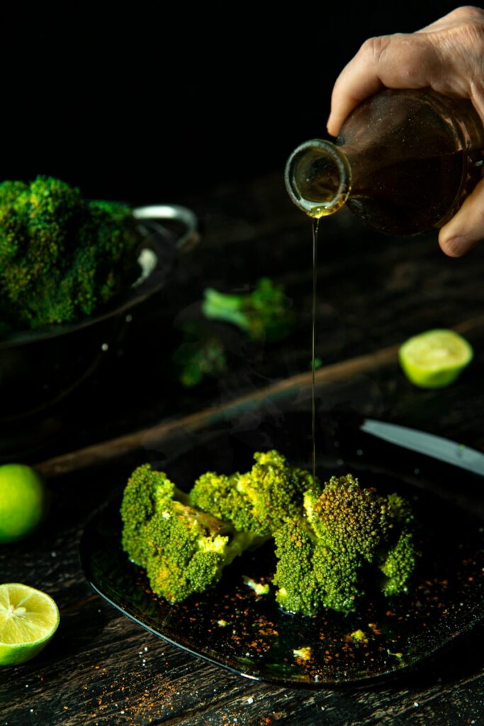 person pouring olive oil on broccoli