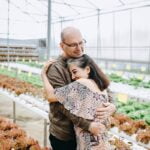 A man and woman embracing in a greenhouse while discussing anti-aging tips.