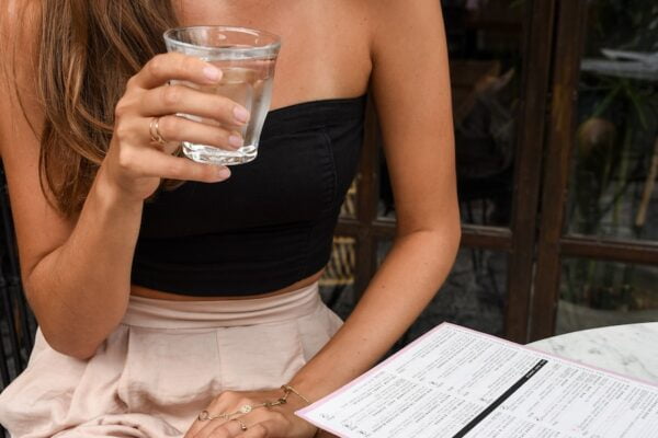 A woman sitting at a table with a glass of water, practicing wellness tips.